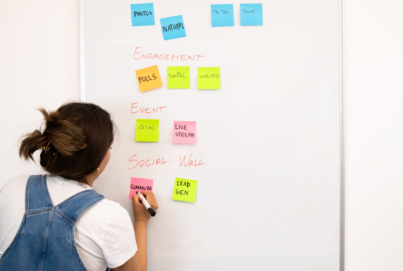 A woman organizing notes on a whiteboard with colorful sticky notes in an office setting.