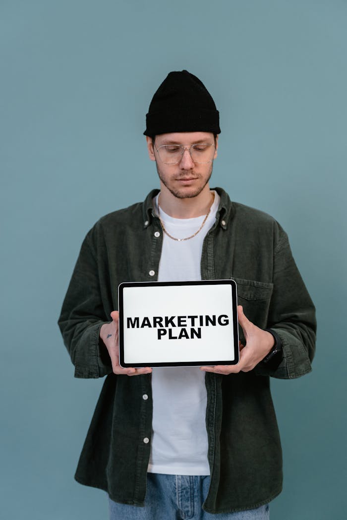 Adult wearing casual clothing holding a tablet that reads 'Marketing Plan'.